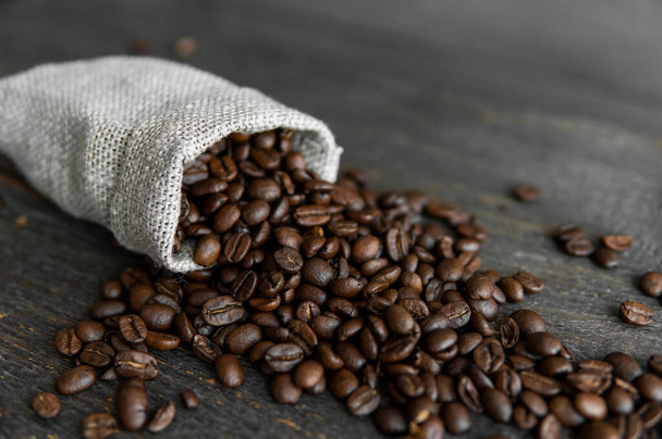 Coffee beans scattered from a linen bag on a wooden table. Fresh roasted arabica coffee beans. - Photo, Image