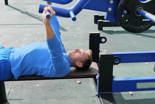 sporty slim man doing bench press using outdoors gym equipment. making an effort to lift a bar. motivation and progress concept. chest exersice. - Photo, Image