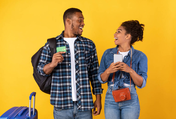 Viajantes excitados cônjuges usando banco móvel em pé sobre fundo amarelo - Foto, Imagem