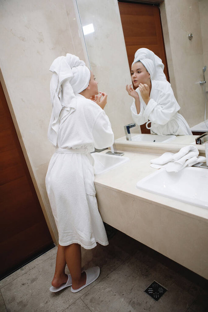 Mladá žena v bílém plášti se umyje v umyvadle kohoutkem v koupelně. Odraz v zrcadle. Vybrané zaměření. - Fotografie, Obrázek