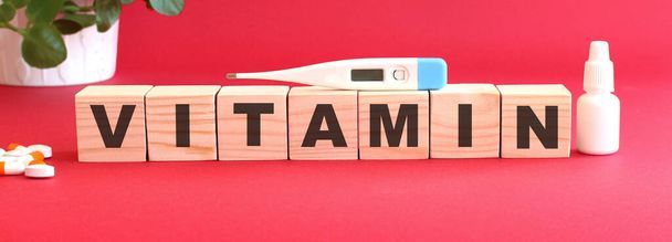 La palabra VITAMINA está hecha de cubos de madera sobre un fondo rojo con medicamentos. - Foto, imagen
