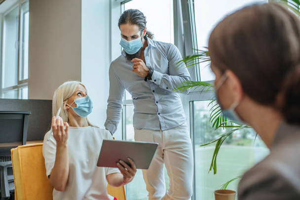 Young business people in protective medical masks discussing something in the office during outbreak of the global pandemic COVID-19. Office life in a new normal. - Foto, afbeelding