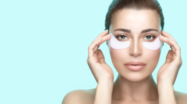 Beauty and skin care concept. Beautiful young woman with healthy fresh clean skin using eye patches.  Anti aging skincare treatment. Eye mask rejuvenation. Turquoise blue background with copy space - Photo, Image