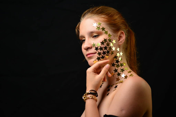Beautiful young woman face close up portrait in studio on black. various emotions. foil stars glued to the face. - Photo, image