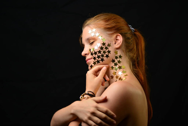 Beautiful young woman face close up portrait in studio on black. various emotions. foil stars glued to the face. - Photo, Image