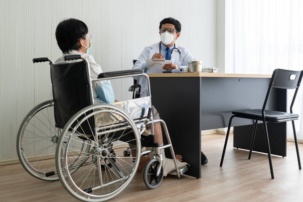 Asijský lékař mluví se starší pacientkou, která má zlomeninu kosti z nehody a sedí na invalidním vozíku. zdravotní péče a lékařské koncepce - Fotografie, Obrázek
