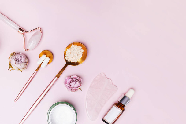 Skincare accessories on pink background. Massage tools, collagen, bottle with serum, face cream. Flat lay. - Foto, immagini