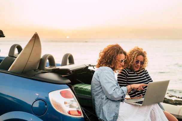 Jonge en mooie vrouw van middelbare leeftijd genieten van reizen en technologie roaming met auto en zonsondergang op de achtergrond  - Foto, afbeelding