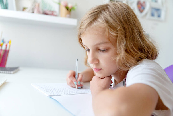 Dziewczyna siedzi przy stole i pisze w notatniku. - Zdjęcie, obraz