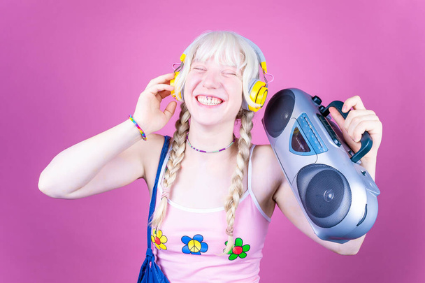 Young beautiful caucasian woman dancing indoor on pink baground holding vintage stereo - Isolated diverse female clubbing holding vintage radio - happiness, excitement, dancing concept - Photo, Image