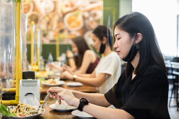 Azjata mężczyzna i kobieta siedzący oddzielone w restauracji jedząc żywność z tarczą stołową przegrody z tworzywa sztucznego w celu ochrony przed zakażeniem koronawirusem covid-19, nowa normalna restauracja i koncepcja odległości społecznej - Zdjęcie, obraz