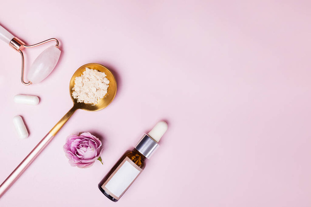 Skincare accessories on pink background. Massage tools, collagen, bottle with serum, face cream. Flat lay. - 写真・画像