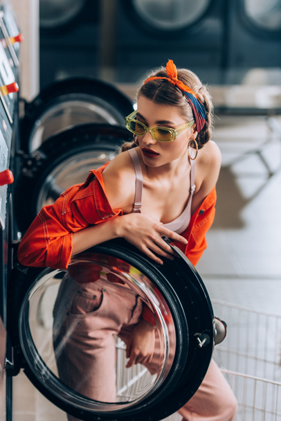 stílusos nő napszemüvegben nézi mosógép a mosodában - Fotó, kép