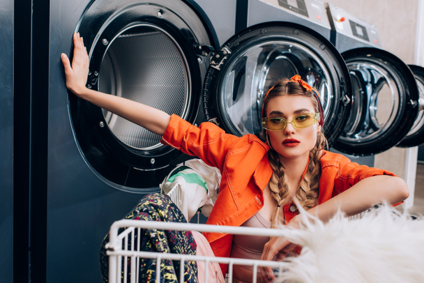 stílusos nő ül a kosárban ruházat közelében mosógép mosodában - Fotó, kép
