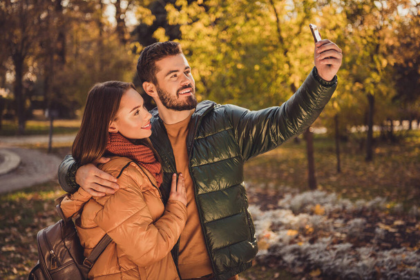 Photo of two people students guy hug girlfriend make selfie on smartphone in fall forest town wear rucksack yellow coats - Фото, зображення
