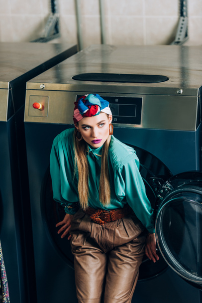 young woman in turban standing near washing machine in laundromat  - Foto, afbeelding