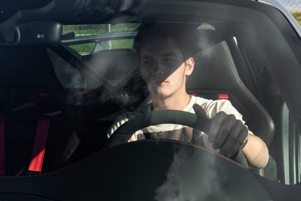 a young man sits behind the wheel of an expensive sports car. guy driving a car. - 写真・画像