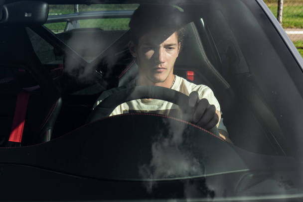Młody mężczyzna siedzi za kierownicą drogiego sportowego samochodu. facet prowadzący samochód. - Zdjęcie, obraz