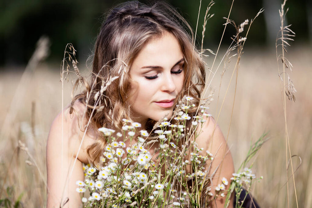 Beautiful young woman in a field among camomiles enjoys nature. Close-up. - Fotografie, Obrázek