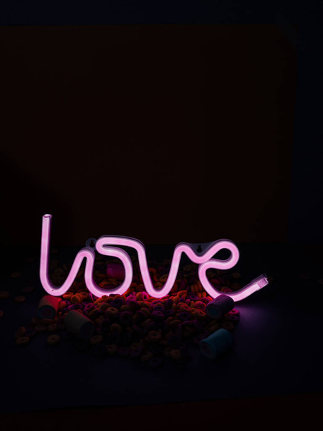 Closeup shot of a neon ''Love'' sign surrounded by marshmallows and colorful cereals - Foto, Bild