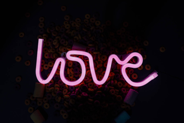 Closeup shot of a neon ''Love'' sign surrounded by marshmallows and colorful cereals - Foto, immagini