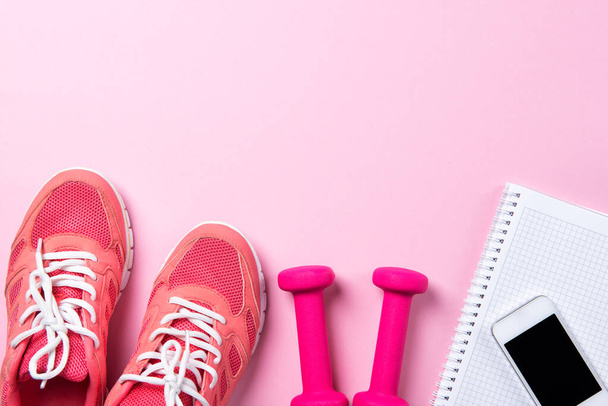Concepto de fitness, zapatillas rosa y mancuernas con portátil con teléfono inteligente sobre fondo rosa, vista superior con espacio para copiar - Foto, Imagen