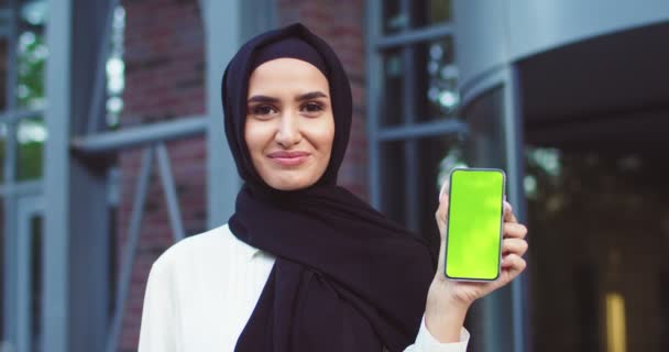 Close up of confident Muslim woman in black hijab holding smartphone with greenscreen. Modern beautiful lady in black traditional headscarves posing outdoors. Islamic happy ladies in classy outfit. - Кадры, видео