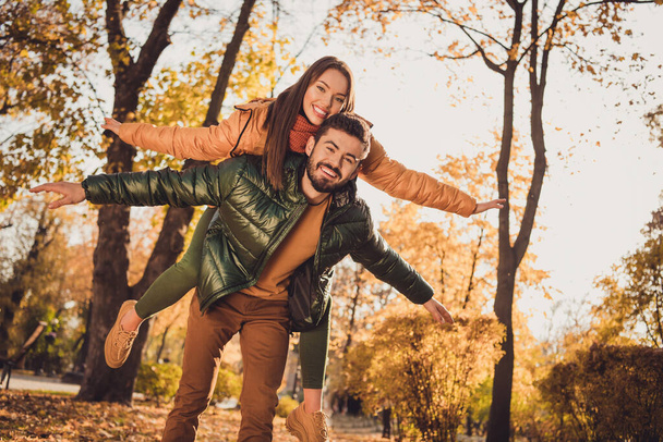 Low angle view photo of romantic couple man carry piggyback girlfriend hold hands in fall city park forest wear coats - Фото, зображення