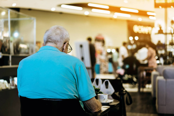 Zadní pohled na starší mužský zákazník pomocí smartphonu, zatímco sedí ve frontě na společenské vzdálenosti pro odnést nápoj v kavárně. Nový koncept normálního životního stylu. - Fotografie, Obrázek
