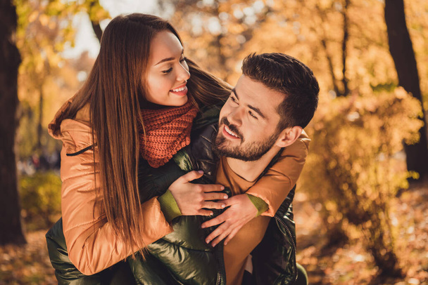 Photo of bonding affectionate couple guy embrace girlfriend piggyback in fall outdoors september city park wear coats - Photo, Image