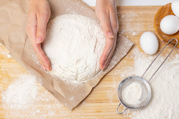 Home cooking concept. Female hands prepare homemade dough on a floured wooden board. Close-up. - Fotoğraf, Görsel