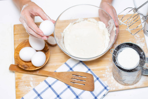 making dough for bread or homemade baked goods. ingredients on the desk. female hands holding an egg - 写真・画像