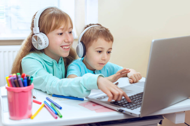 los niños que usan auriculares miran la pantalla del monitor y escriben en el teclado. Lugar de trabajo acogedor, educación en línea, concepto de aprendizaje electrónico, comunicación a distancia con el ordenador portátil - Foto, Imagen