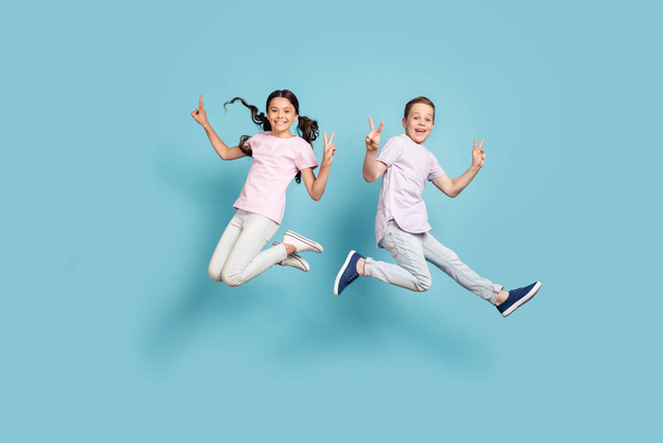 Full length body size view of her she his he nice attractive small little cheerful cheery friends friendship kids jumping showing v-sign having fun isolated over blue pastel color background - Foto, Imagen