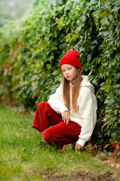 Dívka v běžném podzimním oblečení na rozmazaném rostlinném pozadí - Fotografie, Obrázek