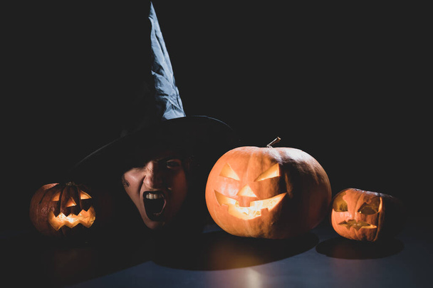 The head of an evil witch is on the table next to the glowing pumpkin jack-o-lantern - Foto, Imagen