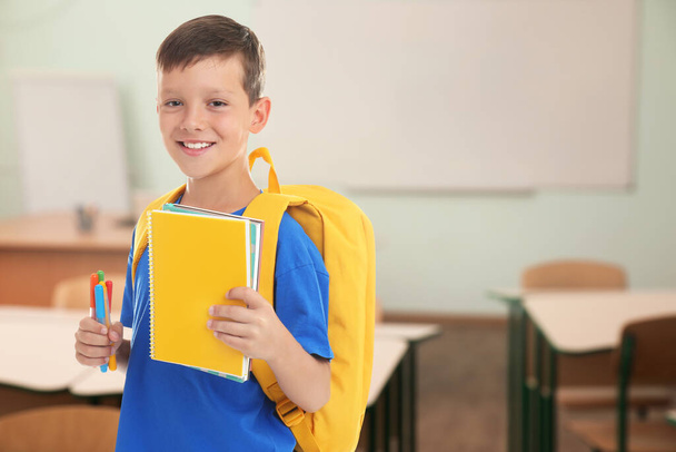 Little boy with school stationery in empty classroom - Фото, изображение