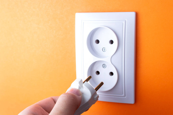 Man steekt stekker in witte stopcontact met twee stekkers op oranje muur - Foto, afbeelding