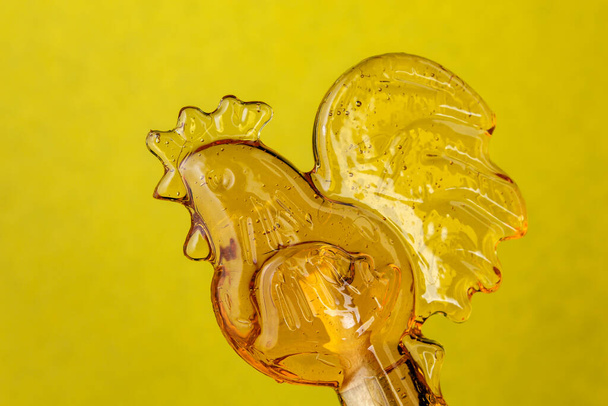 Rooster shaped lollipop, closeup on yellow background. Russian traditional candy in the form of rooster. - Photo, Image