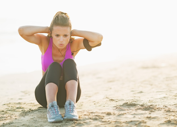Healthy young woman doing abdominal crunch on beach - Foto, afbeelding