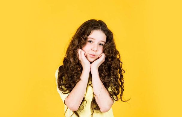Beautiful little model. Healthy curls. Long hair. Easy hairdo. Beauty supplies. Perfectly untangle curly hair. Pretty girl curly hair yellow background. Hairdresser salon. Adorable small child - Fotoğraf, Görsel