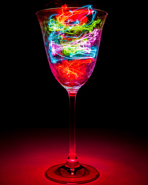 Una sola copa de vino con brillo rojo lleno de relámpagos multicolores. Fondo negro. - Foto, Imagen