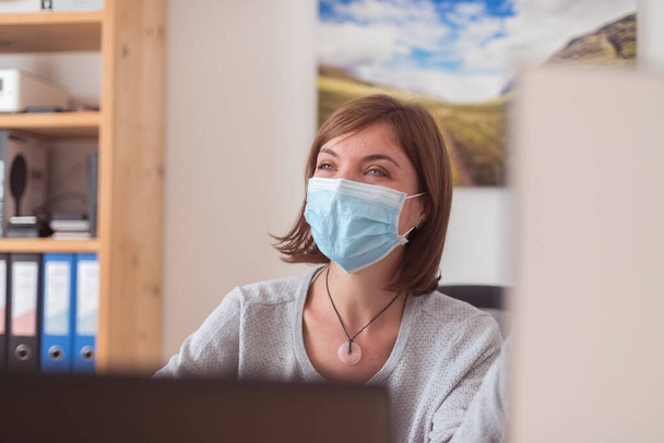 Young woman wearing face mask is working in the office during corona crisis - 写真・画像