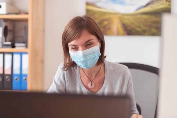 Jovem mulher usando máscara facial está trabalhando no escritório durante crise corona - Foto, Imagem