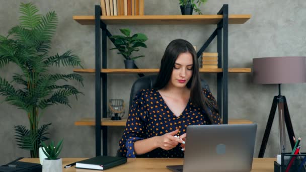 自宅のオフィスで美しいブルネットのビジネス女性マネージャーは、会社の従業員とのリモートオンラインビデオチャット会議コールノートパソコンのコンピュータのウェブカメラに接続する無線イヤフォンに置きます - 映像、動画