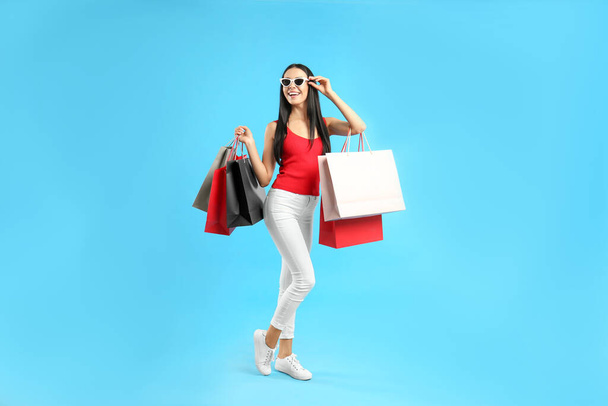 Beautiful young woman with paper shopping bags on light blue background - Φωτογραφία, εικόνα