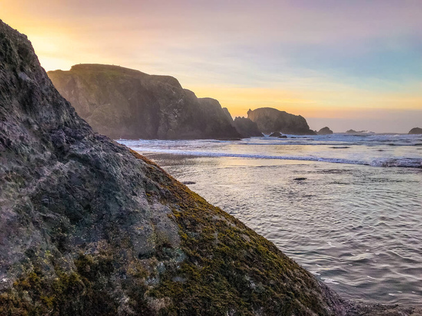 Mossige rots op de voorgrond met zee stapels en oceaan op de achtergrond.  - Foto, afbeelding