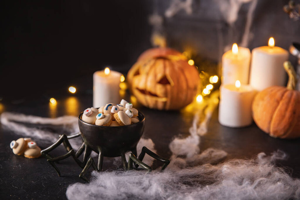 Caramelos y galletas en forma de ojo para las vacaciones de halloween, fondo oscuro con telarañas, calabazas y velas - Foto, imagen
