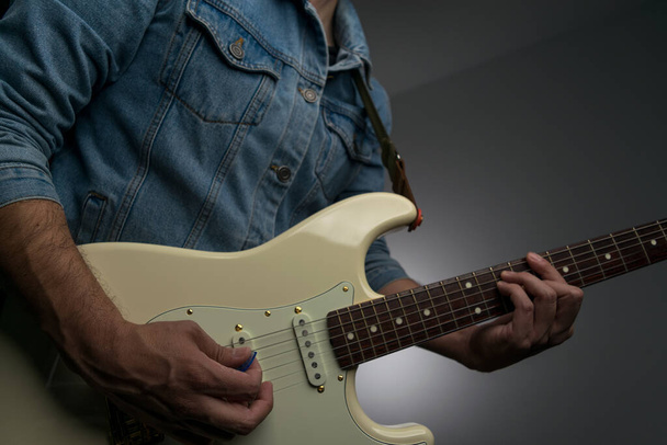 Άνθρωπος παίζει λευκή ηλεκτρική κιθάρα σε ένα τζιν σακάκι - Φωτογραφία, εικόνα