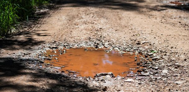 Orangefarbene Pfütze, vom Boden mit Eisen verschmutzt. Berg-Feldweg. - Foto, Bild